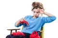 Tortured young girl in a sweater sits on a chair with a red ball of yarn and knitting a scarf and Spitz. Tired. White background.