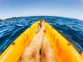 Total lifestyle relax and desconnection concept with men legs in point of view on yellow kayak with blue ocean water around -