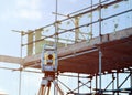 Total station set by engineer on construction site in front of scaffolds installed around house