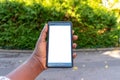 Touch screen mobile phone, in African woman`s hand. Black Female holding smart phone on green outdoor background with blank copy s Royalty Free Stock Photo