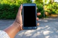 Touch screen mobile phone, in African woman`s hand. Black Female holding smart phone on green outdoor background with blank copy s