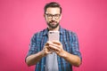 Always in touch. Smiling young man holding smart phone and looking at it. Portrait of a happy man using mobile phone isolated over Royalty Free Stock Photo