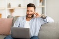 Always in touch. Young freelancer man talking on smartphone and using laptop while working remotely from home Royalty Free Stock Photo