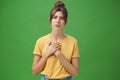 Touched and pleased attractive young woman in yellow t-shirt holding palms pressed to chest in thankful and grateful