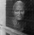 Touching black-and-white photo of an elderly Indian woman looking through a window, capturing the essence of life in an old age