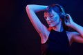 Touching headphones and listening to the music. Studio shot in dark studio with neon light. Portrait of young girl Royalty Free Stock Photo