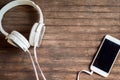 Touchscreen phone on table. White earphones and smartphone on wooden background.