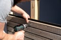 Tough construction worker applies wooden siding to a garage and drills screws