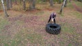 Tough tattooed man bodybuilder hitting the truck tire with a heavy iron hammer - training in the autumn forest