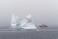 A tour boat passes an iceberg on a foggy day