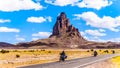 Touring Bike Riders passing the rugged peaks of El Capitan and Agathla Peak towering over the desert landscape of Monument Valley Royalty Free Stock Photo