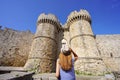 Tourism in Greece. Back view of tourist girl walking down the Marine Gate main entrance to Rhodes town from the harbour, Greece.