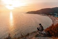 Tourism and sports recreation. A young woman with a tourist backpack on her back sits on a rock and looks at the sunset and the Royalty Free Stock Photo