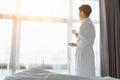 Tourist Asian man in bathrobe towel looking at beautiful scene view on window at hotel room in morning. Traveler Asian man feels Royalty Free Stock Photo