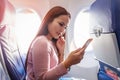 Tourist asian woman sitting near airplane window at sunset and using mobile phone during flight Royalty Free Stock Photo