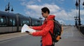 Tourist backpack Asian Man on the street and holding mobile phone and map guide crosswalk a traffic road in the city of Bordeaux Royalty Free Stock Photo