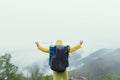 Tourist with a backpack on his back stands on a rock with his hands full and looks at the cloudy mountains from the top, the view