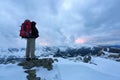 A tourist with a backpack stands on a gray stone.