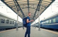 Tourist backpacker with smartphone stand on railway station platform and waiting for train. Travel concept Royalty Free Stock Photo