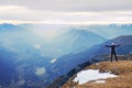 Tourist in black is standing on rocky view point and watching into misty rocky mountains. Fogy winter morning in Alps.. Royalty Free Stock Photo