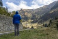 tourist in a blue jacket looks at the road in the mountains, back view. Carpathians, Ridge Fagarash. Transfagarash road Royalty Free Stock Photo