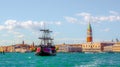 a tourist boating looking like a pirate ship is passing in front of the St. Mark's Square with Campanile and