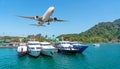 Tourist boats in the bay at the pier of tropical islands with a passenger plane taking off. Travel concept view trip