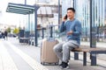 Tourist at the bus station, having fun talking on the phone, sitting on a bench with a large suitcase waiting for a taxi, Asian Royalty Free Stock Photo