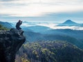 Tourist with camera in hands sit on peak of sandstone rock and watching into colorful mist Royalty Free Stock Photo