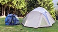 Tourist camp on green meadow with fresh grass in Carpathian mountains forest. Hikers tent and backpacks at camping site. Active l Royalty Free Stock Photo