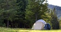 Tourist camp on green meadow with fresh grass in Carpathian mountains forest. Hikers tent and backpacks at camping site. Active li Royalty Free Stock Photo