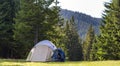 Tourist camp on green meadow with fresh grass in Carpathian mountains forest. Hikers tent and backpacks at camping site. Active li Royalty Free Stock Photo