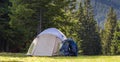 Tourist camp on green meadow with fresh grass in Carpathian mountains forest. Hikers tent and backpacks at camping site. Active li Royalty Free Stock Photo