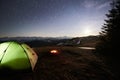 Tourist camping near forest in the mountains. Illuminated tent and campfire under night sky full of stars and the moon Royalty Free Stock Photo