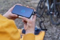 A tourist charges a smartphone with a power bank on the background of a backpack and a bicycle in nature