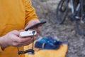 A tourist charges a smartphone with a power bank on the background of a backpack and a bicycle in nature