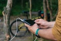 A tourist charges a smartphone with a power bank on the background of a bicycle in forest