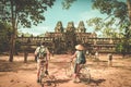 Tourist couple cycling around Angkor temple, Cambodia. Ta Keo building ruins in the jungle. Eco friendly tourism traveling, toned Royalty Free Stock Photo