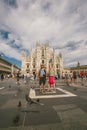 Tourist couple funny posing on the background of the Duomo di Milano on a sunny summer day in the crowd square. Woman handstand at