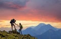 Tourist couple helping each other to climb high rock in evening mountains at sunset Royalty Free Stock Photo