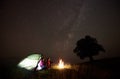 Young couple hikers resting near illuminated tent, camping in mountains at night under starry sky Royalty Free Stock Photo