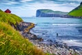 Tourist on a dlack sand beach in Tjornuvik village. Picturesque morning scene of Streymoy island with Eidiskollur cliffs on backgr