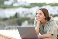 Tourist dreaming with a laptop looking at side in a balcony Royalty Free Stock Photo