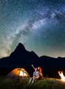 Tourist family - man and woman looking at the shines starry sky at night. Couple hikers sitting near camp and campfire Royalty Free Stock Photo