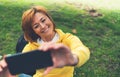 Tourist girl on background green grass taking photo selfie on mobile smart phone, person looking on camera gadget technology Royalty Free Stock Photo