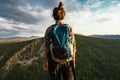 A tourist girl with a backpack admires the sunset from the top of the mountain. A traveler on the background of mountains. Royalty Free Stock Photo
