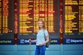 Tourist girl with backpack and carry on luggage in international airport, near flight information board Royalty Free Stock Photo