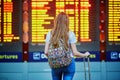 Tourist girl with backpack and carry on luggage in international airport, near flight information board Royalty Free Stock Photo