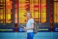 Tourist girl with backpack and carry on luggage in international airport, near flight information board Royalty Free Stock Photo