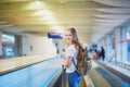 Tourist girl with backpack and carry on luggage in international airport, on travelator